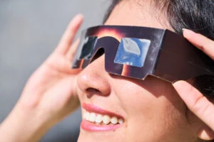 smiling young latin woman watching an eclipse of the sun with eclipse glasses